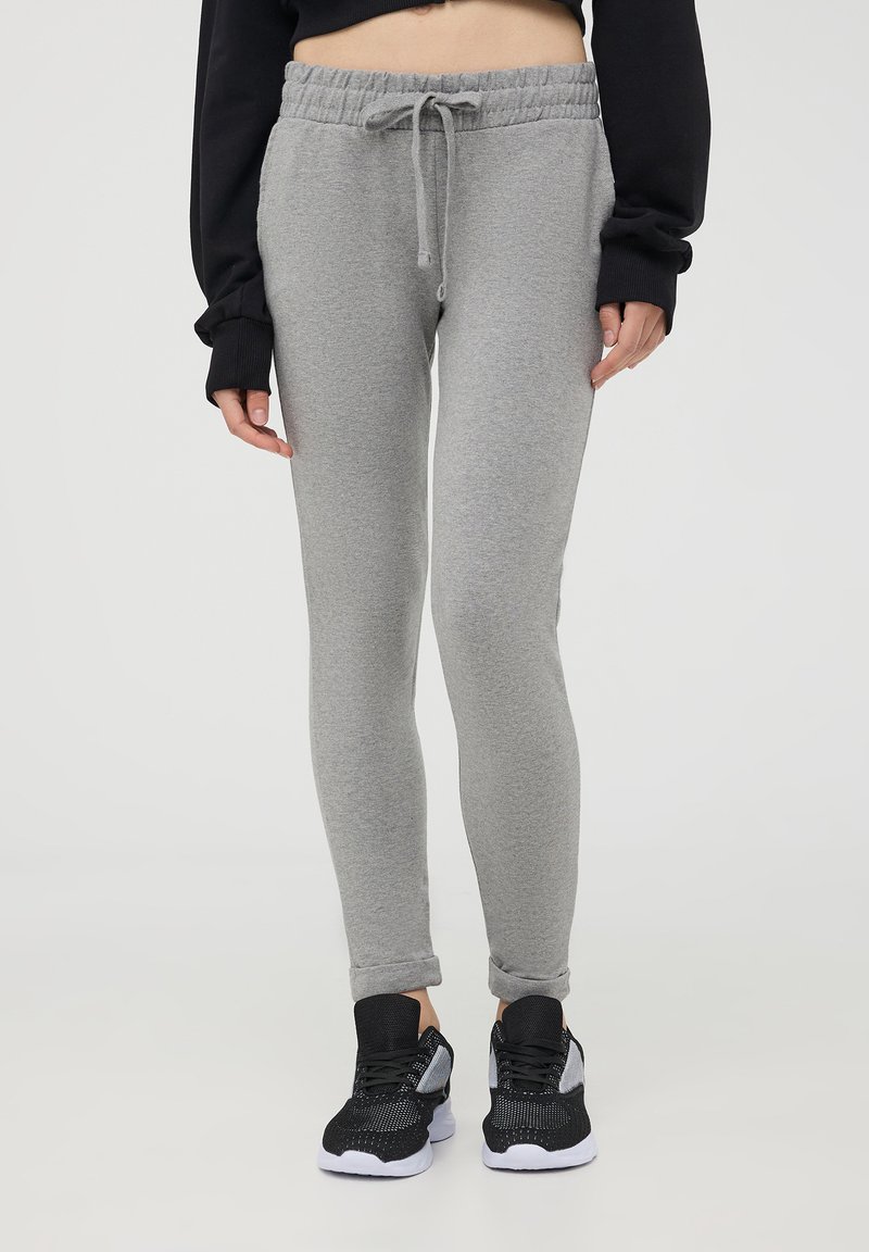 Pantaloni della tuta grigi con vita regolabile, texture liscia, gambe affusolate e polsini elasticizzati. Abbinati a sneakers nere e bianche.