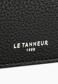 Black leather material with a textured finish. Features embossed white branding "LE TANNEUR 1898" on a flat surface. Simple and understated design.