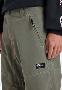 Olive green cargo pants with white stitching, side zip pocket, and logo patch. Made from lightweight fabric, featuring a straight-cut design.