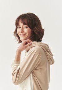 Sudadera con capucha beige con detalles en crema clara. Mangas largas, tejido suave, que cuenta con un corte relajado y un sutil detalle de rayas en los puños.