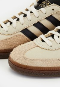 Beige suède sneakers met zwarte leren strepen, gestructureerde tan accenten en crèmekleurige veters. Rubberen zool met een gemêleerd profiel.