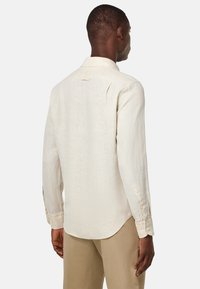 Camicia a maniche lunghe beige chiaro realizzata in lino, con colletto a bottoni, orlo curvo e yoke posteriore con un sottile dettaglio di plissettatura.