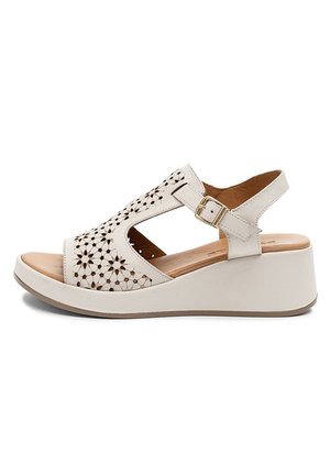 Beżowy sandał na koturnie z kwiatowym wzorem wycięć, regulowany pasek na kostkę z złotą klamrą oraz miękka wkładka.