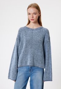 Jasnoniebieski sweter z dzianiny o prążkowanej fakturze, szerokimi rękawami i okrągłym dekoltem, w zestawie z jasnoniebieskimi dżinsami.