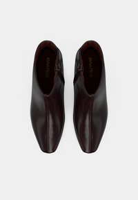 Pár tmavě hnědých kožených kotníkových bot s bočními zipy a čtvercovým designem špičky, zobrazeno z vrchu na bílém pozadí.