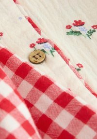 Red and white checked fabric with floral embroidery in red and blue, featuring a natural wooden button and soft, textured cotton material.