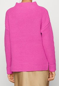 Pull rose tricoté à col montant, épaules tombantes et poignets côtelés. Tissu texturé avec une coupe ample, ourlet arrivant aux hanches.