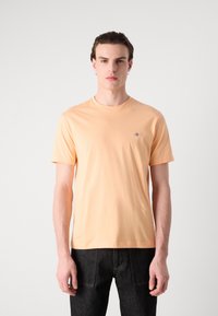 Kortærmet T-shirt med rund halsudskæring i lys ferskenfarvet bomuld, med et lille broderet logo på venstre bryst. Glat tekstur.