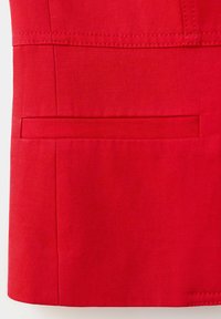 Gros plan d’un vêtement en tissu rouge montrant une poche horizontale fendue avec des coutures visibles et des coutures nettes.