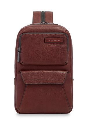 Zaino a tracolla in pelle marrone con due tasche frontali, una con zip e una con patta, con etichetta "THE BRIDGE" sulla tasca superiore.