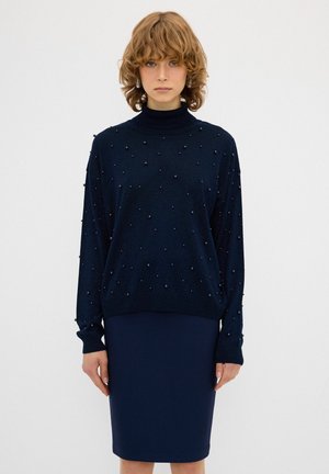 Mørkeblå sweater med høj hals, prydet med små dekorative perler. Matchende tætsiddende mørkeblå blyantskirt. Blødt stof med behagelig tekstur.