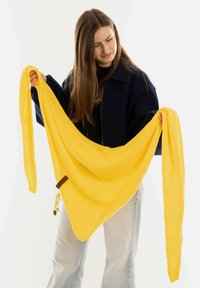 Gele gebreide sjaal met een driehoekige vorm, open geweven textuur, met een bruine accent aan de onderkant en een trekkoorddetail.