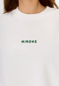 Felpa bianca con colletto rotondo, caratterizzata da scritte ricamate in verde che recitano "MIRONS" sul davanti. Tessuto dalla consistenza liscia.