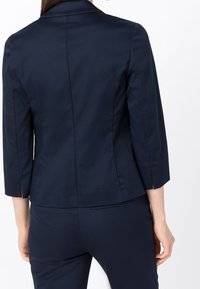 Navy blue, fitted blazer with three-quarter sleeves, tailored back, subtle sheen, side slits, and clean lines for a professional appearance.