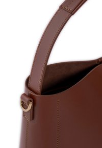 Braune Lederhandtasche mit runder Form, featuring glatter Textur, goldenen Hardware-Akzenten und sauberer Naht entlang der Kanten.