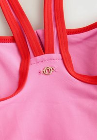 Top rosa con spalline rosse, una texture liscia e un piccolo accento dorato al centro. Design semplice con colori a contrasto.