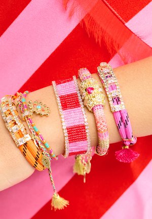 Bracelets multicolores avec différentes textures et formes, ornés de perles, strass et pompons dans des tons de rose, orange et or.