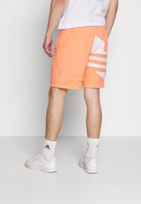 Oranssit shortsit, joissa on rakenteellinen kangas ja valkoiset vinoviivat vasemmalla puolella. Yhdistetty valkoisiin kenkiin ja sukkiin sporttisen ilmeen luomiseksi.