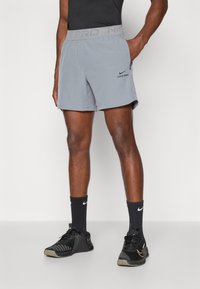 Šedé športové šortky Nike Pro s elastickým pásom, ktorý obsahuje vyrazený text "NIKE PRO", bočné vrecká a ľahký materiál.