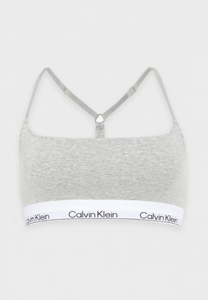 Ανοιχτό γκρι bralette Calvin Klein με ρυθμιζόμενους γκρι ιμάντες και λευκή ελαστική ταινία με μαύρα λογότυπα Calvin Klein.
