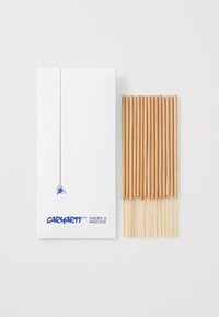 Des bâtonnets d'encens dans une boîte blanche avec un graphique d'araignée bleue. Les bâtonnets sont marron clair, avec une texture lisse et une forme cylindrique.
