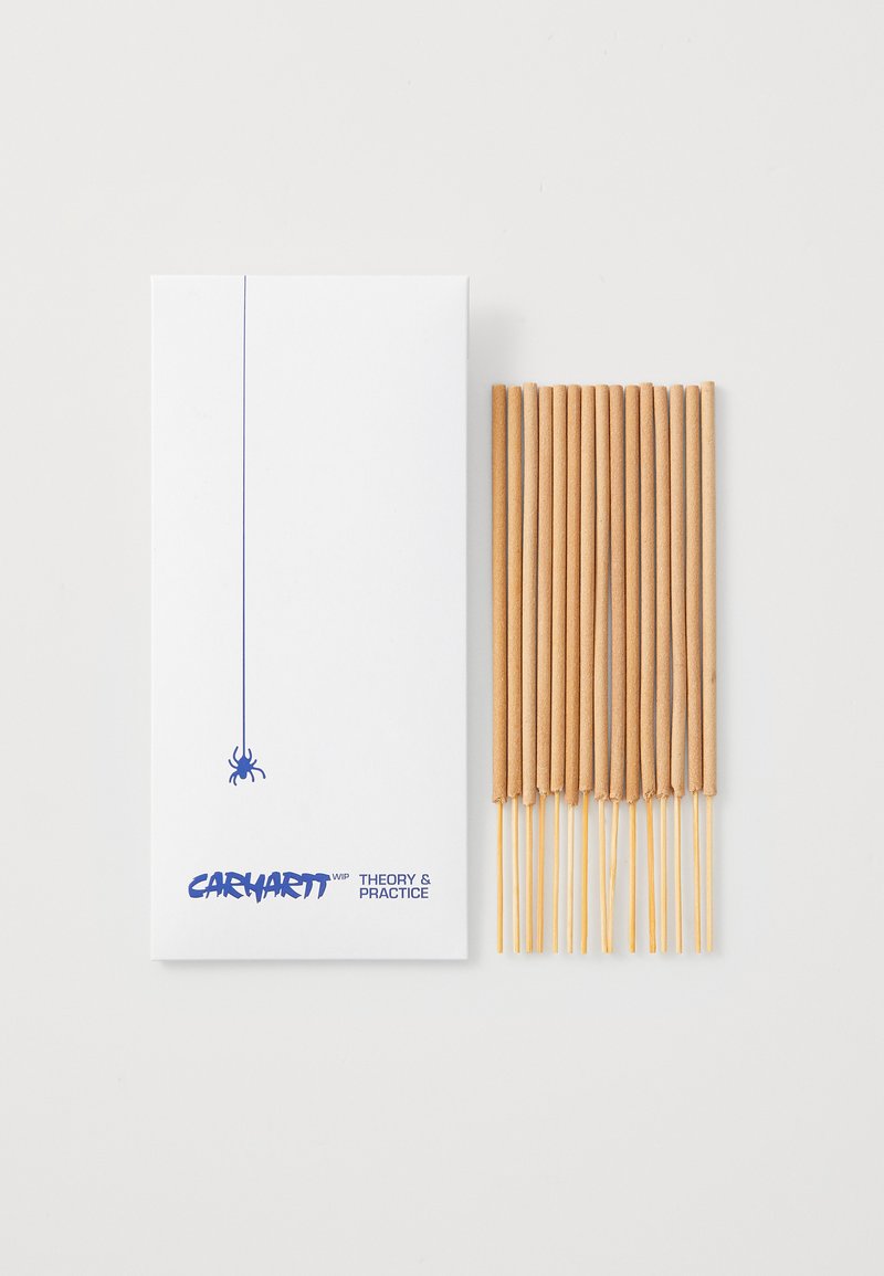 Incense sticks in a white box featuring a blue spider graphic. The sticks are light brown, with a smooth texture and cylindrical shape.