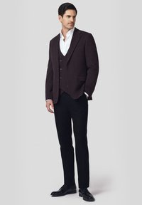 Ciemnofioletowa marynarka na dopasowanej kamizelce z trzema guzikami, biała koszula pod spodem oraz wąskie czarne spodnie połączone z czarnymi butami.