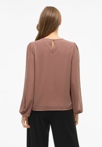 Blusa a maniche lunghe in rosa polveroso, realizzata in tessuto morbido. Presenta un collo rotondo e un dettaglio a occhio di bue sul retro. Design fluido, con accenti minimi.