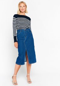Falda midi de mezclilla azul con abertura frontal, combinada con una blusa de rayas en navy y blanco de manga larga, que presenta detalles de botones en las mangas.