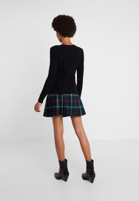 Svart kabelstickad tröja kombinerad med en plisserad rutig kjol i mörkgrönt, marinblått och rött. Svarta ankelstövlar kompletterar outfiten.