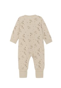 Beige bomullsoverall med en upprepande kaninprint, långa ärmar och muddar vid anklarna. Mjuk textur med avslappnad passform.