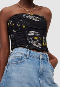 Haut sans bretelles noir à motif floral avec texture froncée et détails de coutures visibles, associé à un short en jean taille haute bleu clair.