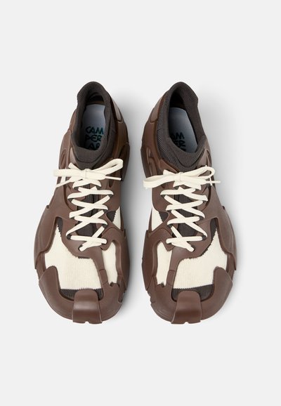 Scarpe da ginnastica marroni e crema con una tomaia texturizzata, robusti accenti in gomma e lacci in contrasto. Presentano un design unico e stampato.
