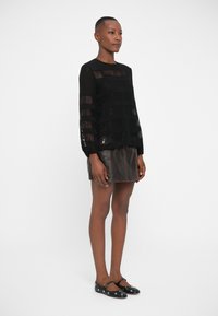 Svart gjennomsiktig bluse med horisontale striper, paret med et brunt skinn miniskjørt. Svart ballet flats med sølvdetaljer.