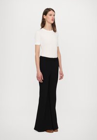 White short-sleeve T-shirt paired with high-waisted black trousers. Trousers have a flared design and smooth texture. Brown shoes complete the look.