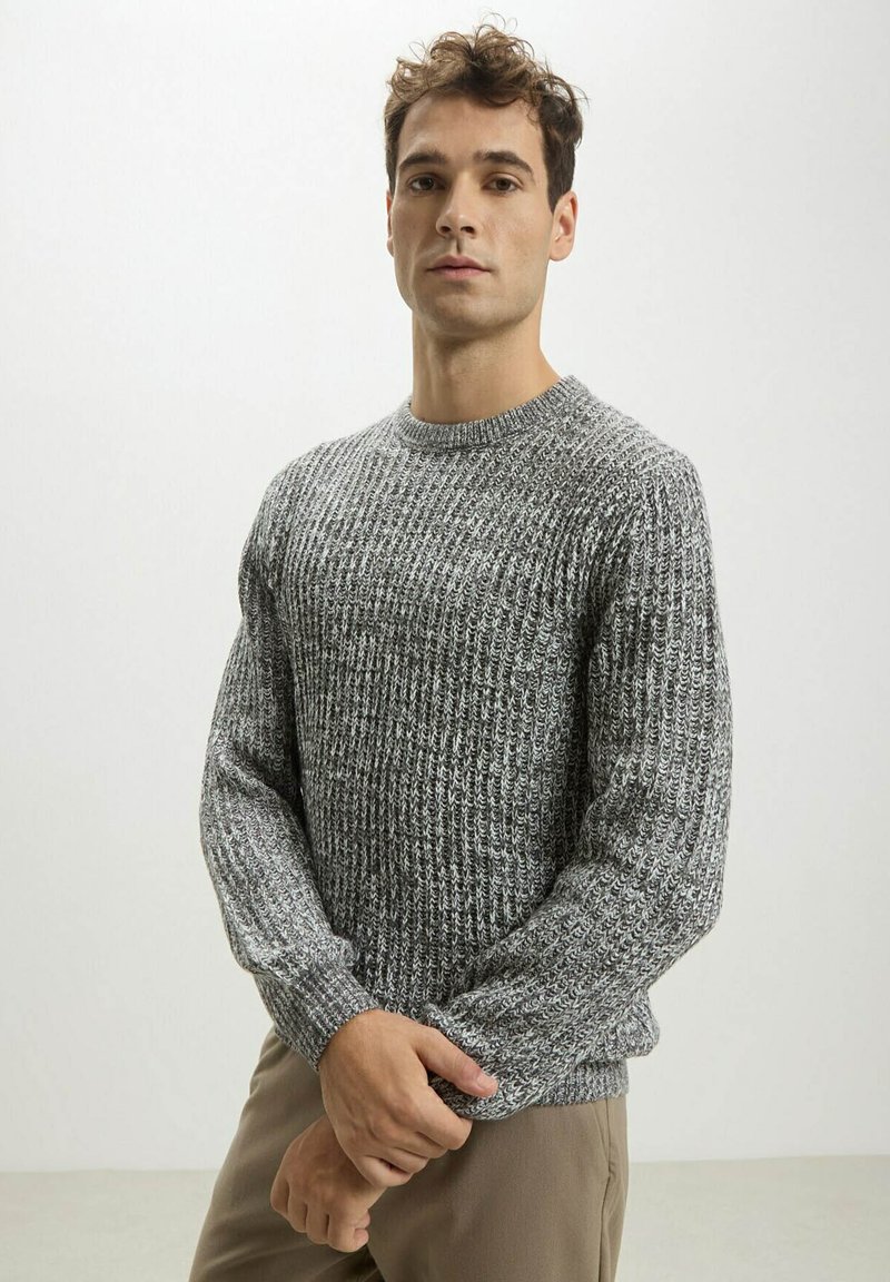 Maglione grigio a maglia con motivo testurizzato, scollatura tonda e maniche lunghe. Il tessuto ha un aspetto morbido e ricco, abbinato a pantaloni beige.