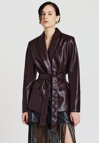 Burgunderfarbener Lederblazer mit taillierter Taille, Reverskragen und zwei vorderen Taschen. Glatte Textur mit einer figurbetonten Silhouette.