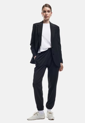 Zwart op maat gemaakte blazer over een wit T-shirt, gecombineerd met zwarte joggerpants en witte sneakers. Gladde stof met een relaxte pasvorm.