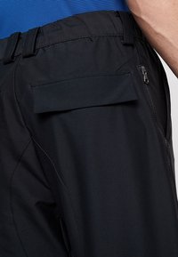 Černé kalhoty s hladkým povrchem, vybavené kapsou na zip a plochou zadní kapsou. Elastický pas a štíhlý střih.