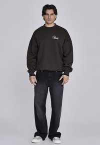 Czarny sweatshirt w ciemnym odcieniu z prążkowanymi mankietami i kołnierzem, z małym białym logo. W połączeniu z luźnymi, ciemnymi dżinsami i białymi trampkami.