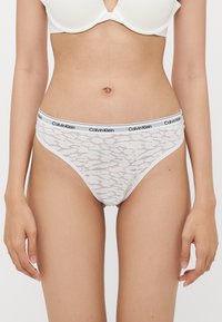 Witte kanten slip met een Calvin Klein logo tailleband. Heeft een bloemenpatroon en een lage taille. Zachte textuur en delicate vormgeving.