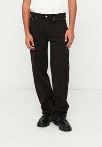 Pantalons noirs à jambes droites en coton résistant. Dotés d'une fermeture à bouton, de cinq poches et de quincaillerie en ton argent. Texture lisse.