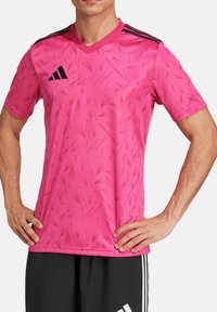 Roze sporttrui met een gestructureerd driehoekig patroon, korte mouwen en een V-hals. Voorzien van zwarte schouderstrepen en logo.