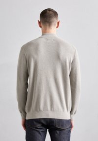 Pull en maille côtelée gris avec manches longues, col rond et ourlet légèrement élastique, associé à un jean en denim foncé.