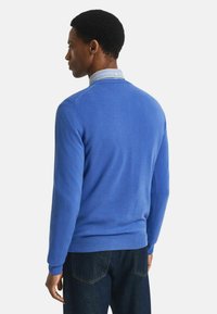 Blauer Strickpullover mit rundem Ausschnitt, langen Ärmeln und gerippten Bündchen. Wird über einem Hemd mit Kragen getragen und zeigt einen strukturierten Stoff.