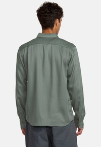 Langarmshirt in een gedempte olijfgroene stof met een gladde textuur, met knoopmanchetten en een klassieke kraag. De achterkant toont een ontspannen pasvorm.