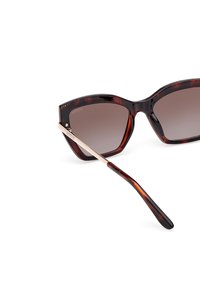 Occhiali da sole oversize tartarugati con lenti marroni sfumate. Presentano un'accennato in metallo dorato sulla stanghetta e bordi eleganti e curvi.