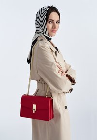 Czerwona skórzana torebka na ramię z złotym łańcuszkiem, prostokątny kształt, gładka struktura, z klapką i wyraźnym logo marki.