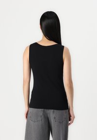 Black sleeveless top with a rounded neckline, made of smooth fabric. Worn with light gray, high-waisted, wide-leg jeans with back pockets.
