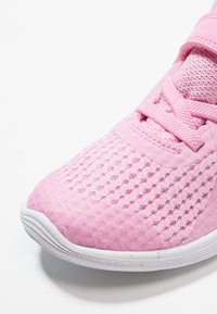 Sportovní obuv z jemné růžové síťoviny se strukturovaným vzorem, s plochou bílou gumovou podrážkou a odpovídajícími růžovými tkaničkami.